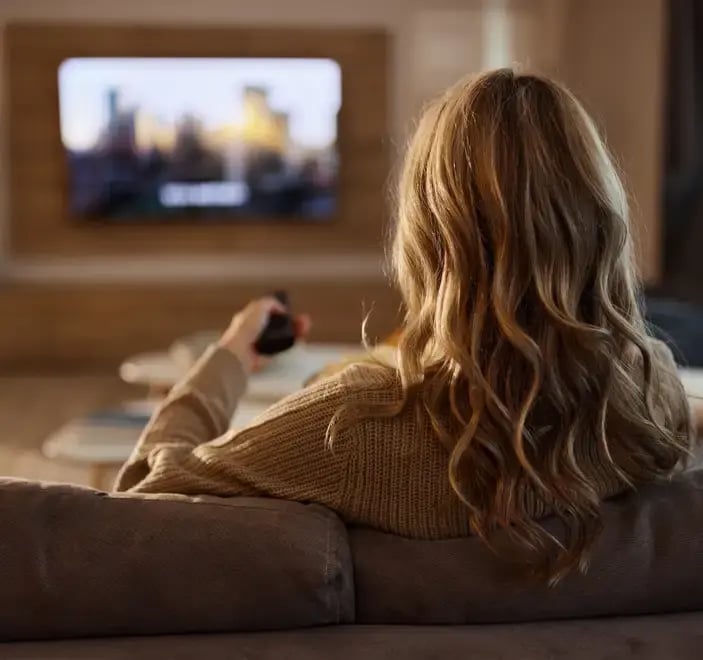 Back of a woman changing the TV channel with her remote.
